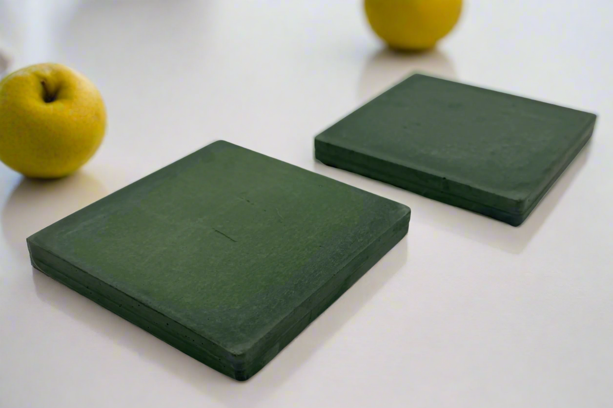 Pair of handcrafted square concrete coasters in deep dark green. Modern rustic style, shown on white background.