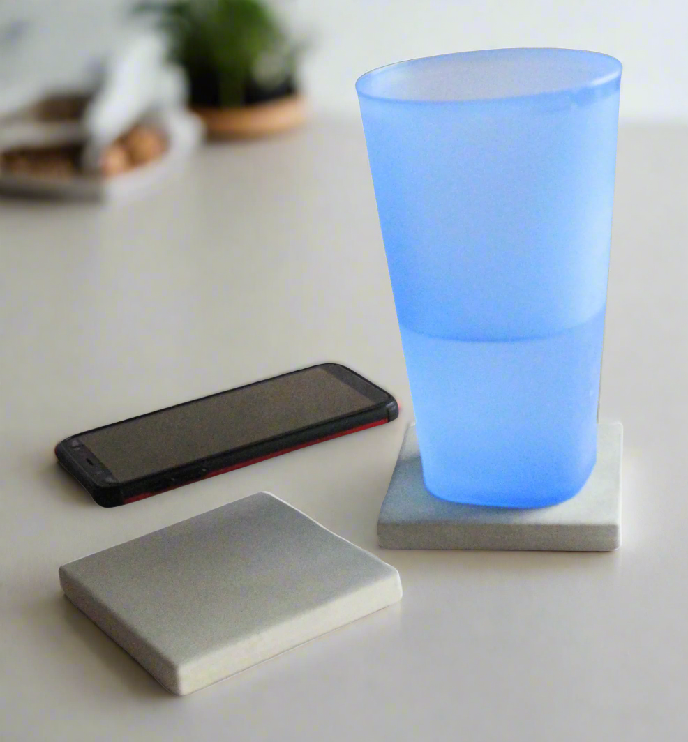 Two handcrafted grey concrete coasters protecting surface under blue cup, beside cell phone. Modern rustic style.