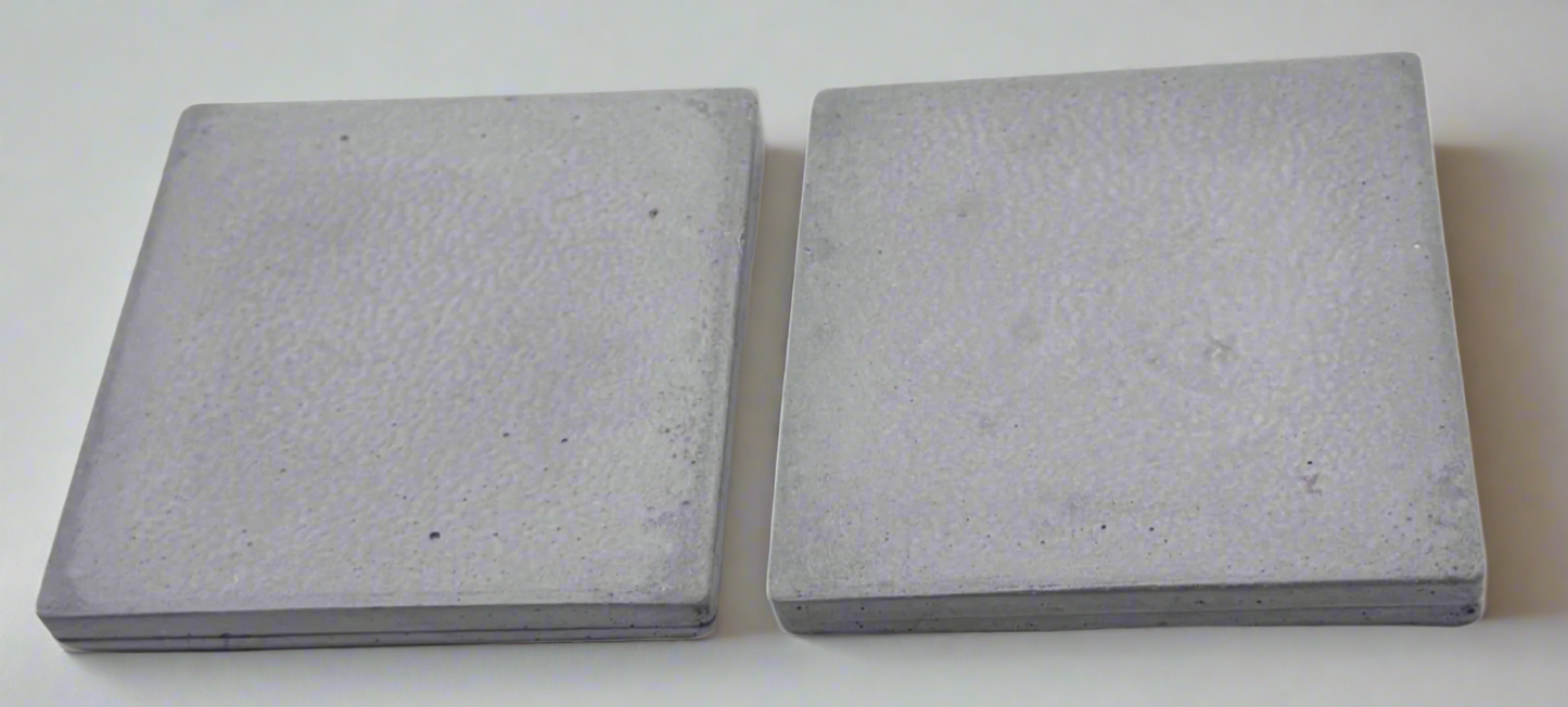Two concrete grey square concrete coasters on white background. Handcrafted modern rustic design.