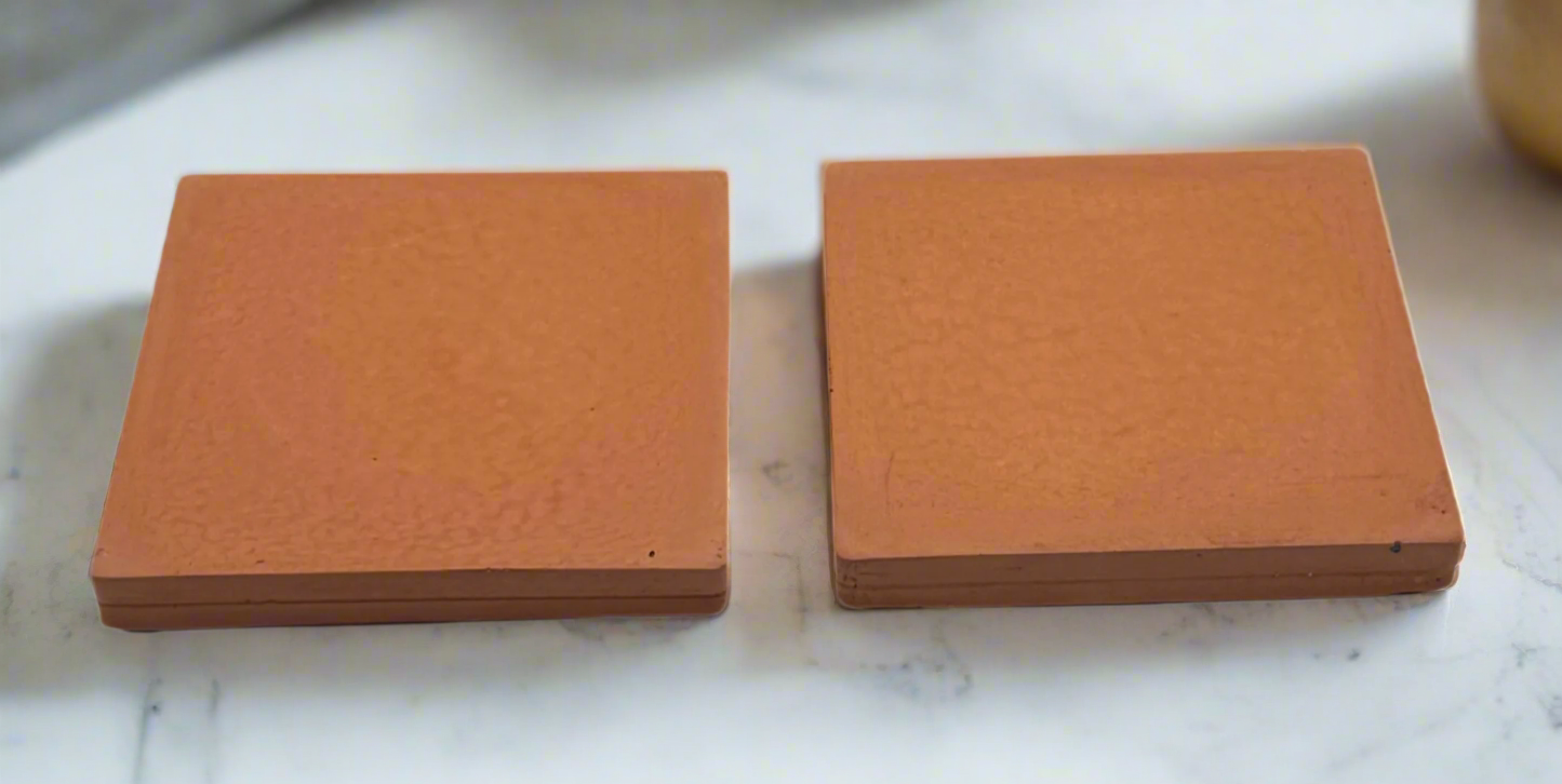 Two squash orange square concrete coasters on white background. Handcrafted modern rustic design.