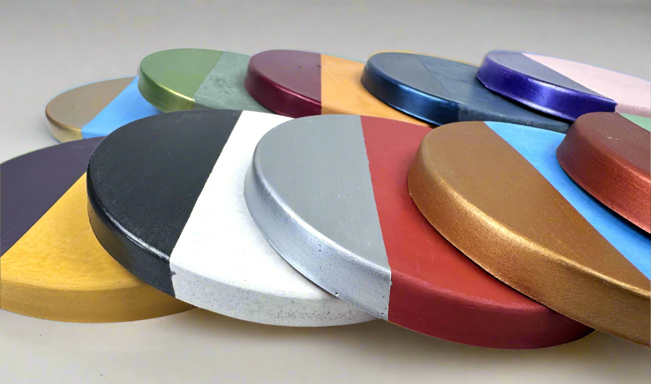 A diverse collection of round concrete coasters is displayed against a white background, each featuring a unique combination of cement base color and a semi-circular hand-painted accent in shades of gold, silver, copper, blue, green, purple, and red, showcasing the customization options.