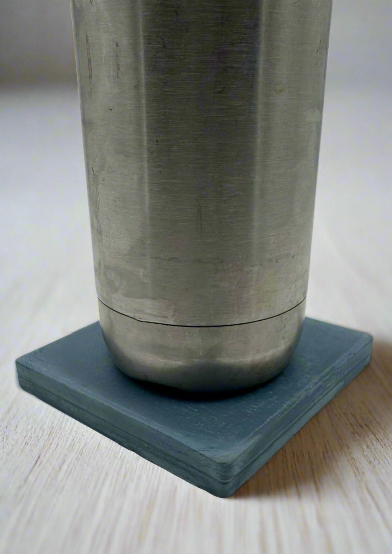 Dark blue square concrete coaster holding a silver cup on white background. Handcrafted modern rustic style.
