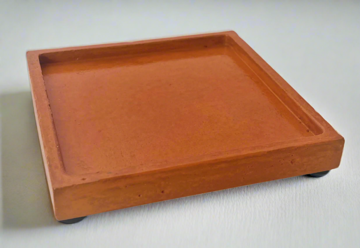 A single glossy Coral square concrete coaster tray with four small black felt pads on its underside is angled on a white background.