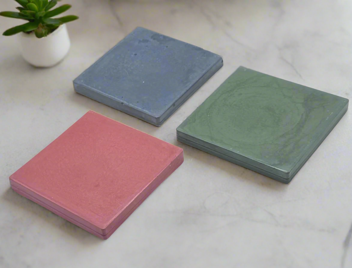 Three glossy square concrete coasters in Dark Blue, Dark Green, and Blush Pink are arranged diagonally on a white background.