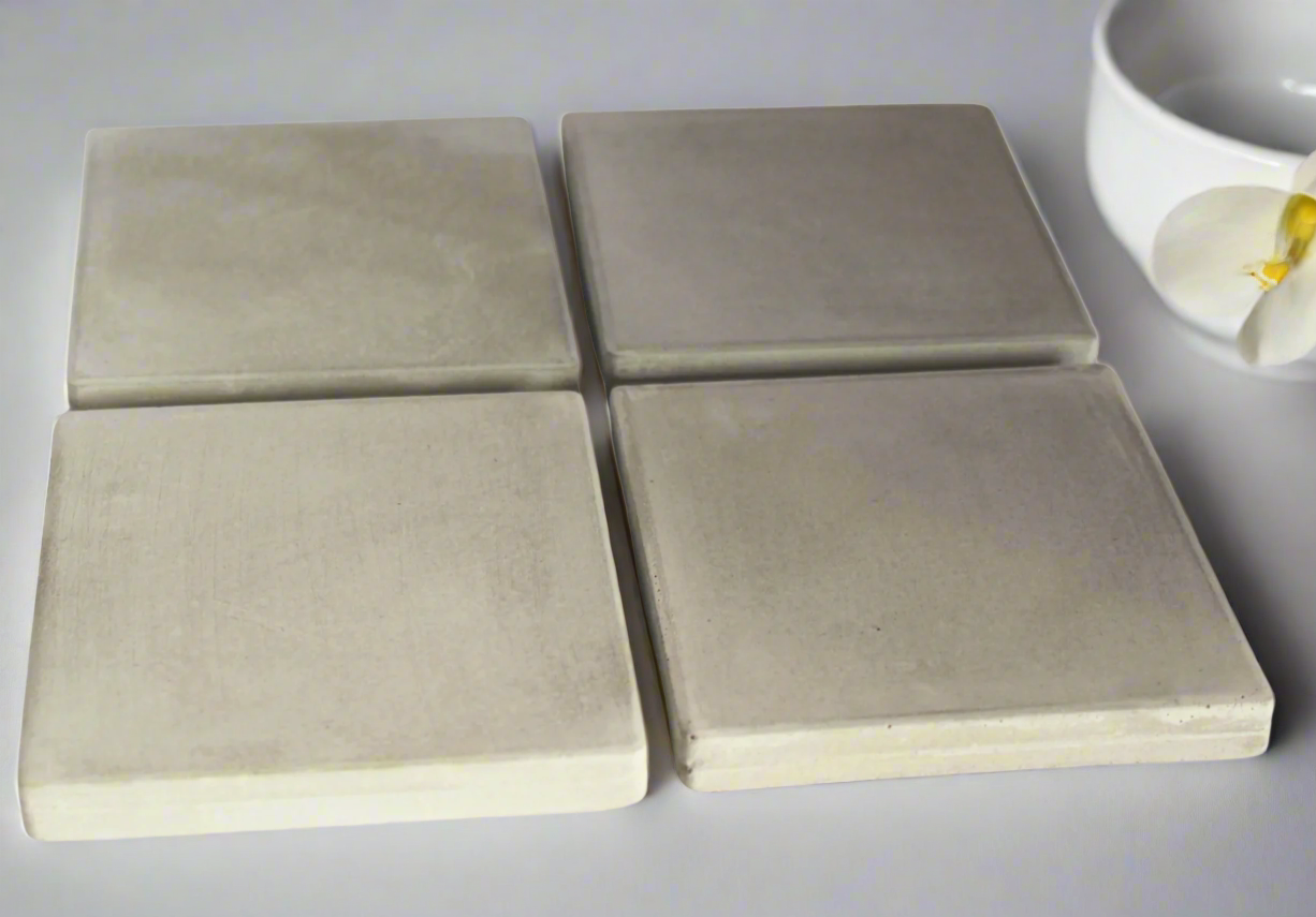 Four square grey concrete coasters displayed. Handcrafted modern rustic style provides surface protection.