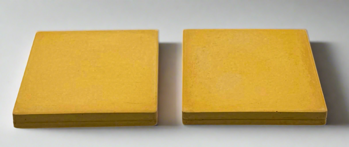 Pair of handcrafted square concrete coasters in rich mustard yellow. Modern rustic, white background.