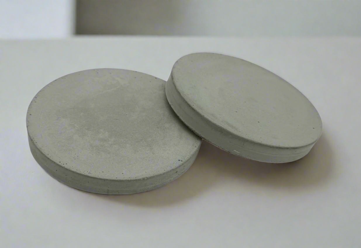 Close-up of two round cement gray concrete coasters. Both face up, one tilted slightly against the other. Modern rustic design.