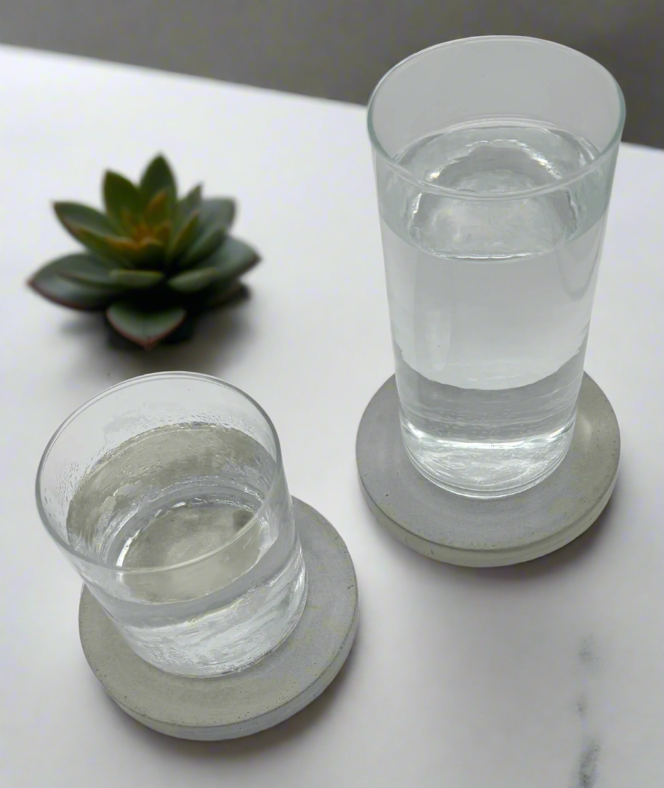 Set of two round cement gray concrete coasters in use, each supporting a glass of water of different heights.