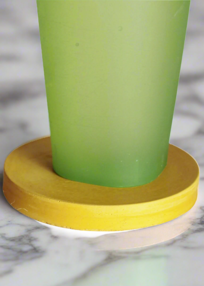 A frosted green glass sits on a round handmade concrete drink coaster in Mustard Yellow against a white background, showcasing the coaster's circular shape and absorbent material.