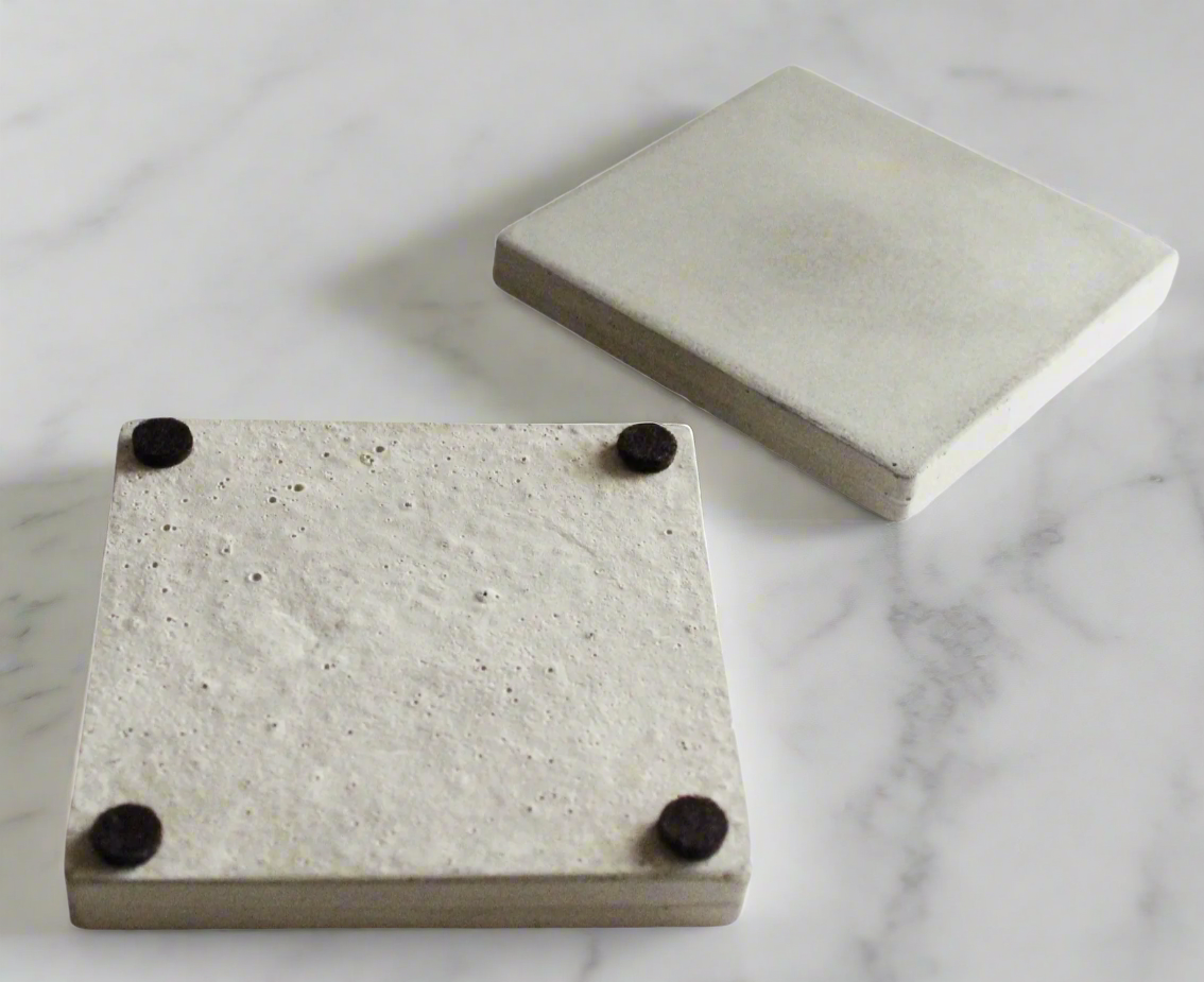 White square concrete coasters (2): one reveals underside with 4 protective felt feet. Handcrafted modern style.
